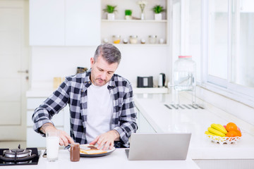 Mature man making breakfast while working