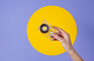Female hand holding audio cassette on purple background with yellow circle