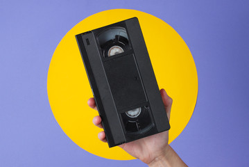 Female hand holding video cassette on purple background with yellow circle