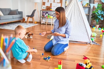 Young caucasian child playing at playschool with teacher. Playing with toy soldiers at playroom around toys.