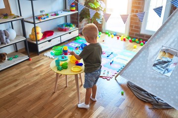Young caucasian kid playing at kindergarten with toys. Preschooler boy happy at playroom.