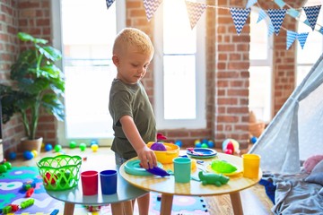 Young caucasian kid playing at kindergarten with toys. Preschooler boy happy at playroom.