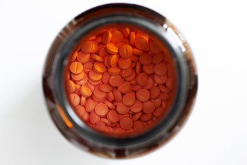 orange round tablets in white classic glass jar in medical healthcare drugstore concept,closed up