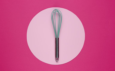 Kitchen whisk on a pink background with pastel color circle in the middle. Top view. Minimalism