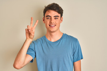 Naklejka premium Teenager boy wearing casual t-shirt standing over isolated background smiling with happy face winking at the camera doing victory sign. Number two.