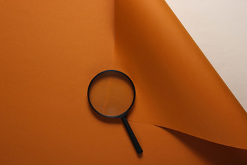 Magnifier on brown paper background. Top view