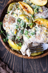 Chicken thighs roasted with apples and cider on a dark brown wooden table. Fall dinner recipe. Comfort food.