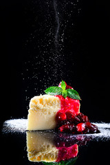 cherry cheesecake on a black background with reflection and flying icing sugar
