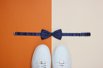 Stylish white sneaker and bow-tie on two-color paper background. Minimalistic fashion concept. Top...