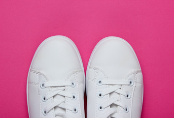 Stylish white sneakers on pink paper background with pink circle. Minimalistic fashion concept. Top view