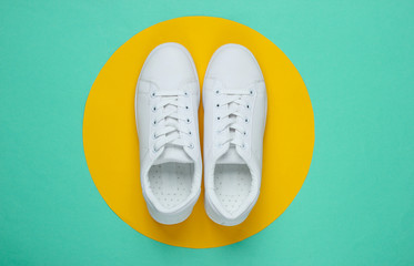 Stylish white sneakers on blue paper background with yellow circle. Minimalistic fashion concept. Top view