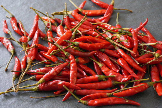 Close-up image of a pile of hot Thai bird chiles on a gray slate background