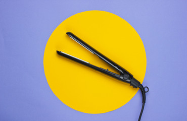 Hair straightener on a purple background with yellow circle in the middle. Top view. Minimalistic beauty and fashion concept