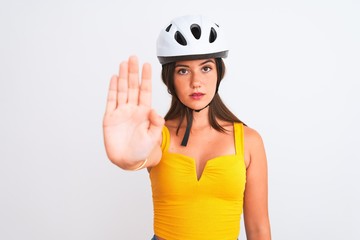 Young beautiful cyclist girl wearing bike helmet standing over isolated white background with open hand doing stop sign with serious and confident expression, defense gesture