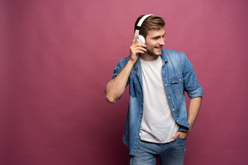 Portrait of happy young man listening to music with headphones isolated over pink background.