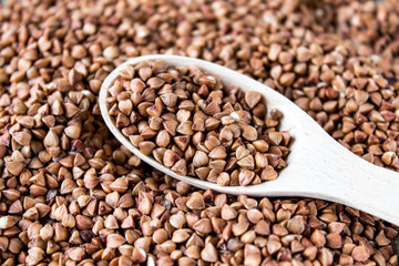 Raw buckwheat in a spoon on a pile of scattered buckwheat. Buckwheat is used for cooking.