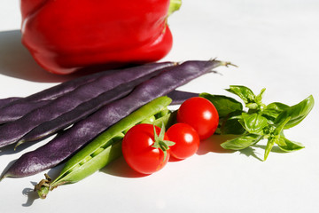 cherry tomatoes, green Basil leaves, pea pods, purple bean pods and red bell peppers. Seasonal vegetables on white background