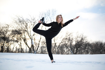 Young caucasian female blonde in leggings stretching exercise on open air in snowy forest. fit and sports lifestyle