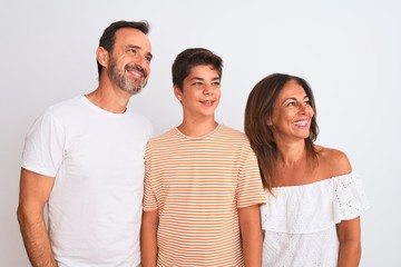 Family of three, mother, father and son standing over white isolated background looking away to side with smile on face, natural expression. Laughing confident.