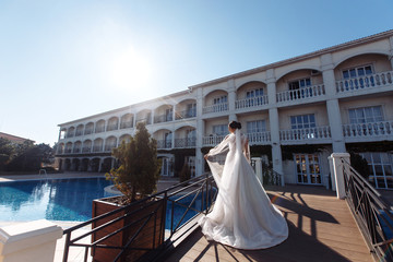 Obraz premium Beautiful sexy bride in white dress posing near the pool. Happy bride in luxurious wedding dress posing in the sunshine. Wind blows her veil. Wedding day. Marriage. Fashion bride.