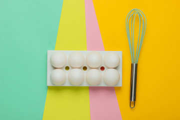 Tray with white chicken eggs and whisk on colored background. Minimalistic food concept. Top view