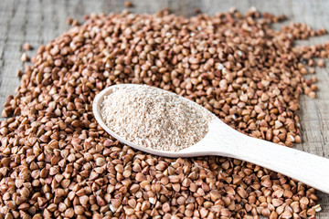 Buckwheat flour in a wooden spoon on a pile of roasted buckwheat. A pile of buckwheat flour.