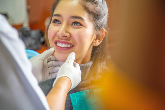 Dentist examining teeth of beautiful young smiling Asian woman in hospital clinic dental health care concept