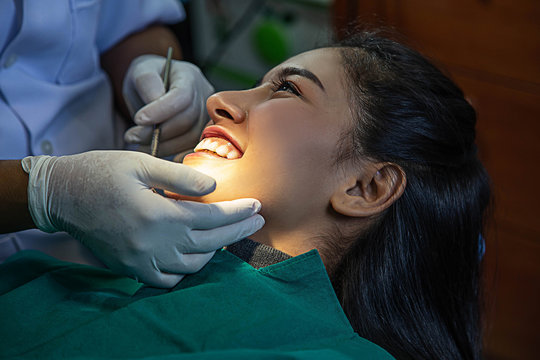 Dentist examining teeth of beautiful young smiling Asian woman in hospital clinic dental health care concept