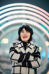 Happy brunette girl with plaid coat and black hat on background of glowing circle