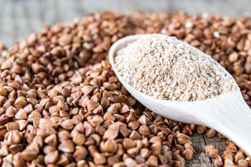 Buckwheat flour in a wooden spoon on a pile of roasted buckwheat. A pile of buckwheat flour.
