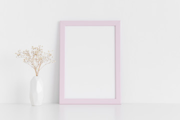 Pink frame mockup with a gypsophila in a vase on a white table.Portrait orientation.