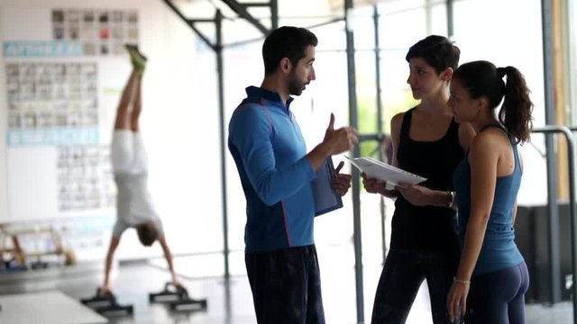 Gym instructor assisting two sporty women  in fitness center.Concept of exercises 