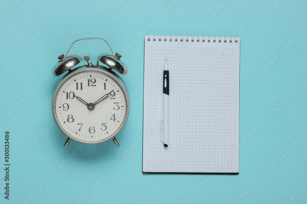 Poster Notebook with an alarm clock on blue background. Minimalistic business concept. Top view