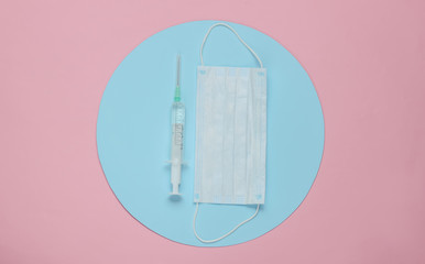 Fototapeta na wymiar Syringe and medical mask on pink background with blue circle in the middle. Minimalistic medical concept.