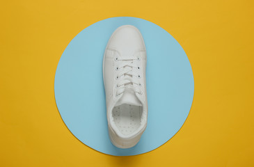Stylish white sneaker on a yellow background with blue circle in the middle. Top view. Minimalism...