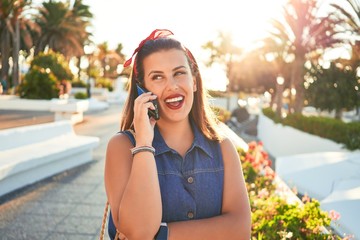 Young beautiful woman smiling happy walking on city streets on a sunny day of summer doing a phone call with smartphone