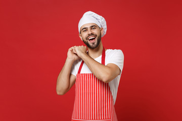 Funny young bearded male chef cook or baker man in striped apron white t-shirt toque chefs hat posing isolated on red background in studio. Cooking food concept. Mock up copy space. Clenching fists.