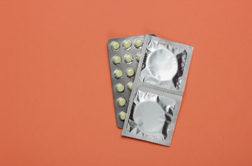 Condoms in packaging, birth control pills on pink background. Top view. The concept of sexual preservation
