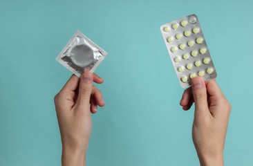 Hand holds condoms in packaging, birth control pills on blue  background. Top view. The concept of...
