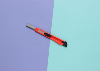 Stationery knife for cutting paper on colored background. Top view