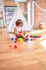 Beautiful toddler wearing glasses and unicorn diadem sitting playing with building blocks at kindergarten