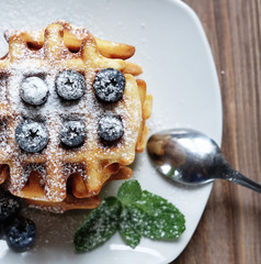 Homemade waffles with blueberries in plate on wooden table