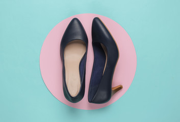 Classic women’s high heel shoes on a blue background with a pastel pink circle in the middle. Stylish shoes. Minimalistic fashion still life. Top view