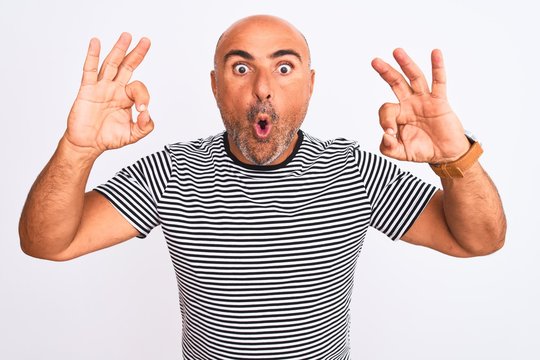 Middle age handsome man wearing striped navy t-shirt over isolated white background looking surprised and shocked doing ok approval symbol with fingers. Crazy expression