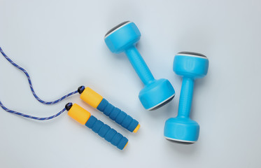 Minimalistic sport still life. Skipping rope and.dumbbells on white background. Top view