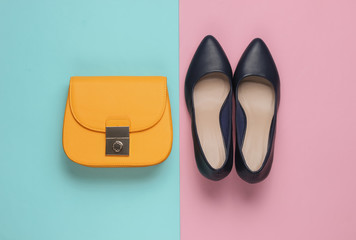 Minimalistic fashion still life. Classic women’s high heel shoes, yellow leather bag on pink background.