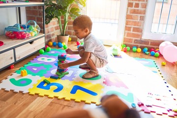 Beautiful african american toddler playing with wooden blocks building tower smiling at kindergarten