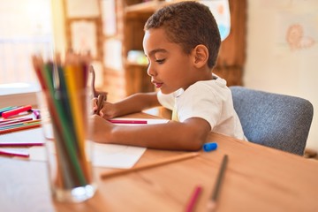 Beautiful african american toddler sitting painting car toy using marker pen on desk at kindergarten