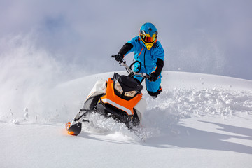 the guy turns a snowmobile in a mountain valley on the background of the clear snow and sky, leaving behind a trail of splashes. bright snow bike and suit without brands. Boondocker sports snowmobile