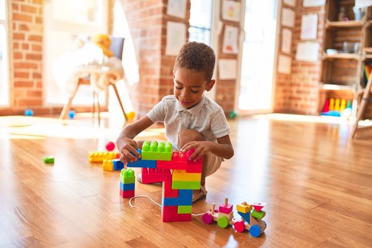 Beautiful african american toddler playing with building blocks smiling at kindergarten